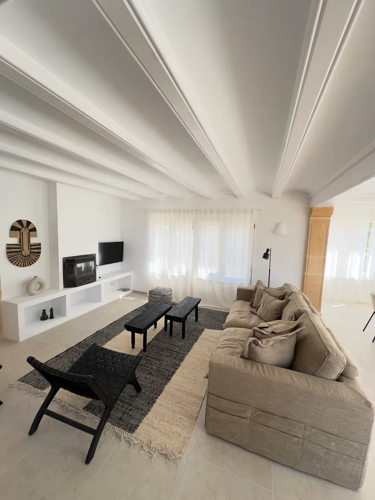 Salón de villa en Jávea con techo de vigas blancas y chimenea